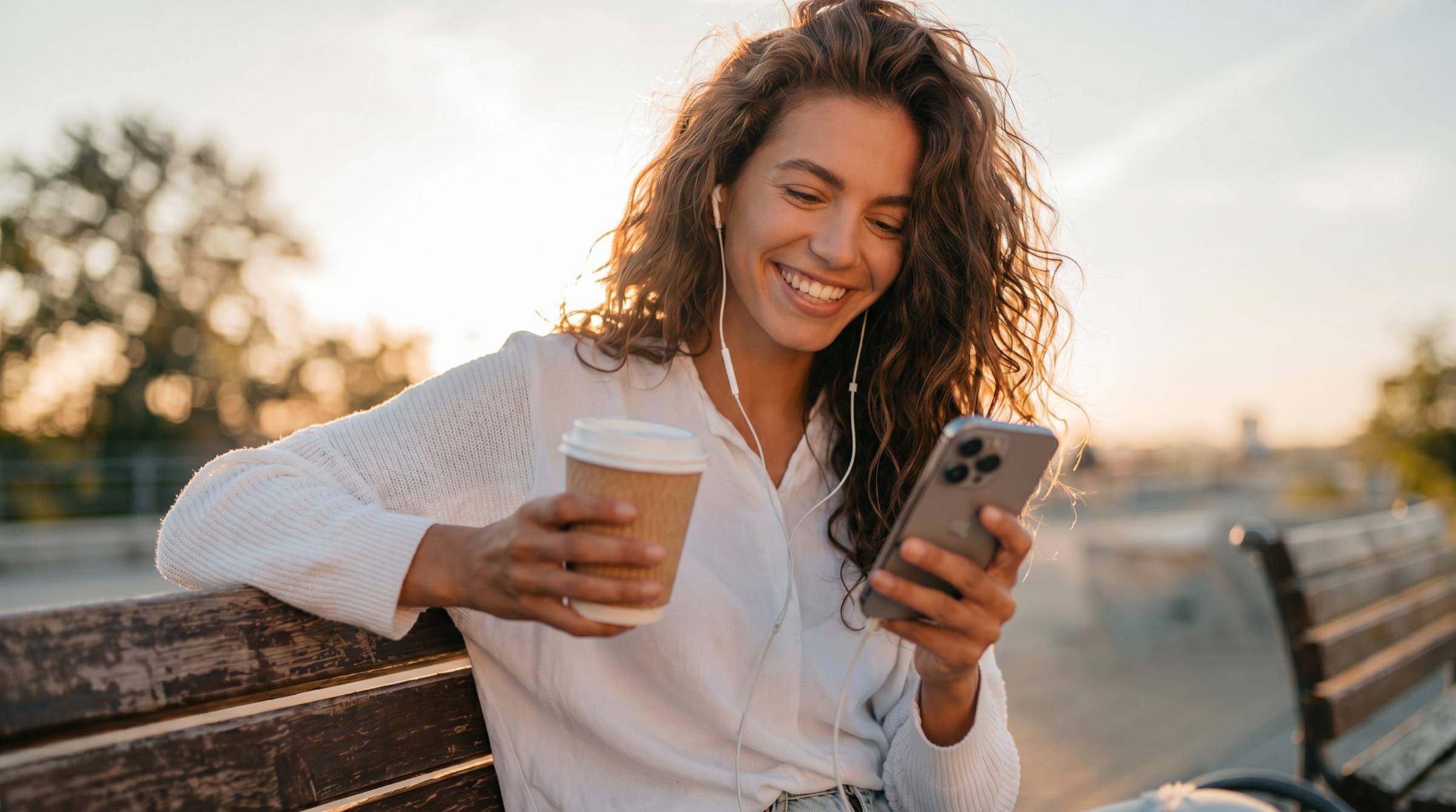 A smiling woman sitting outdoors with a coffee, talking on her phone
